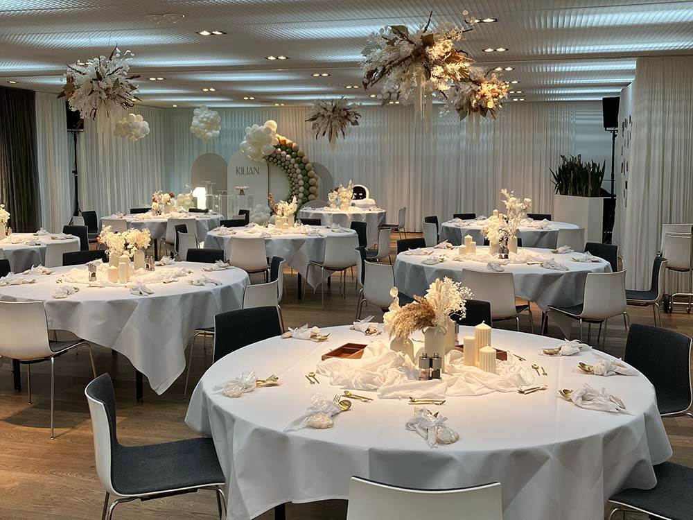 Elegant birthday decorations with tables laid in white and decorated with delicate flowers, golden cutlery and candles.